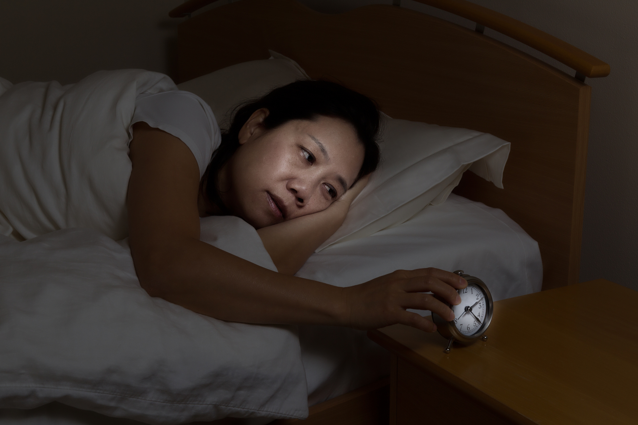 Woman in bed with eyes open touching clock on nightstand