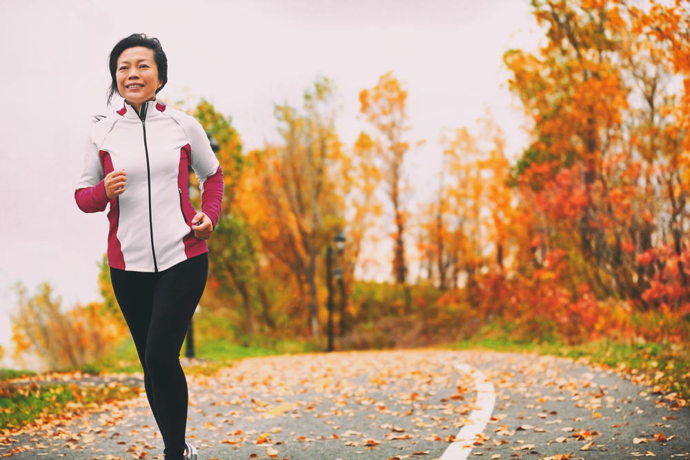 Mature Asian woman running in a park among colorful fall foliage