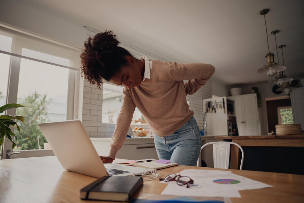 Young woman standing and holding back while working on laptop at home Young woman standing and holding back while working on laptop at home