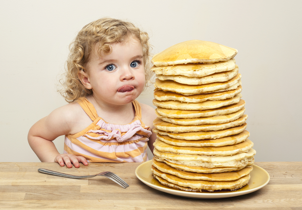 Young girl licking her lips and eying a huge stack of pancakes Young girl licking her lips and eying a huge stack of pancakes