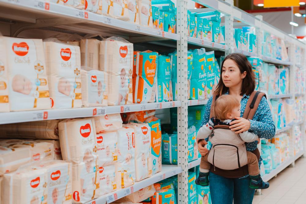 Mother picking out diapers at a store with a baby in a sling