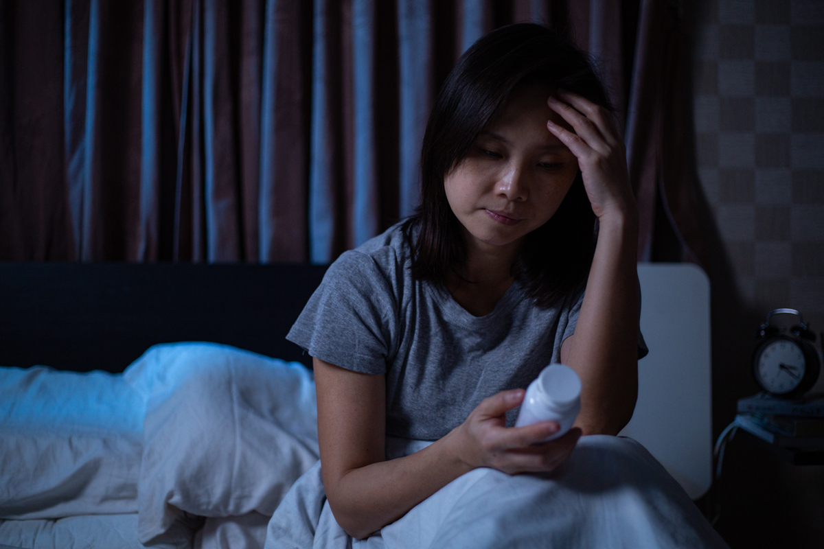 Woman sitting up in bed and looking at a pill bottle.