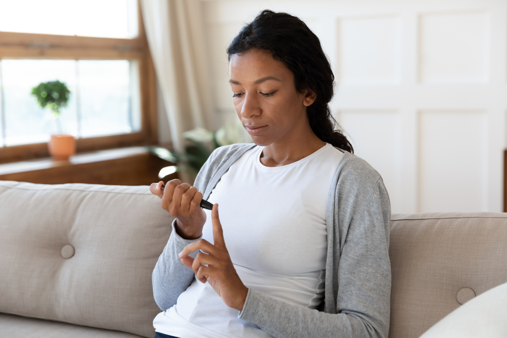 Young woman sitting on a couch doing a glucose test