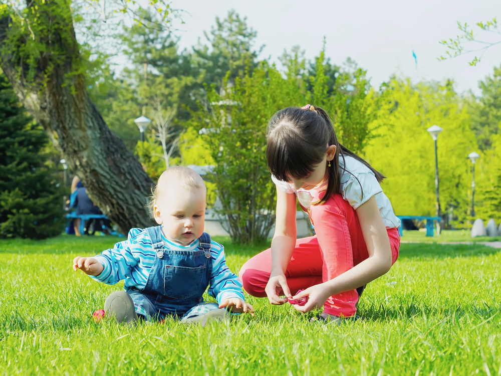 Infant boy and older sister playing in the grass