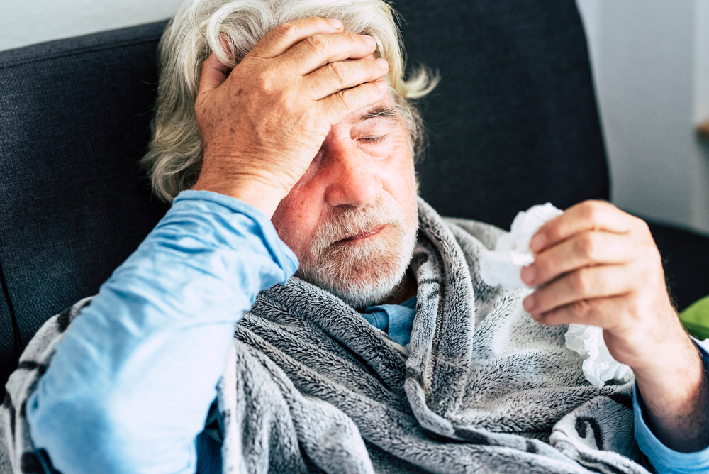 Older man holding his head with one hand and a tissue in the other Older man holding his head with one hand and a tissue in the other