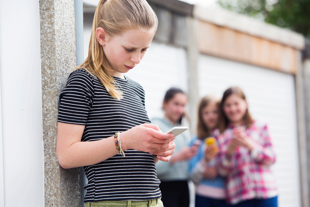 Preteen girl looking at phone while three girls laugh in the background