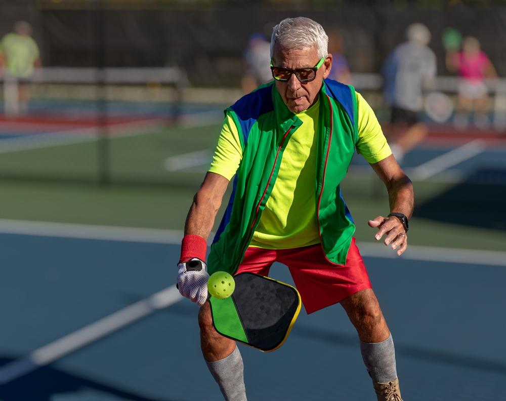 Senior man hitting a pickleball with paddle