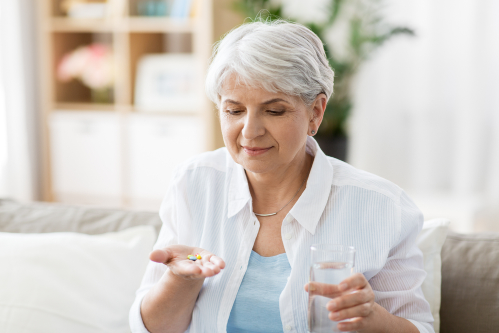Senior woman taking pills with glass of water at home