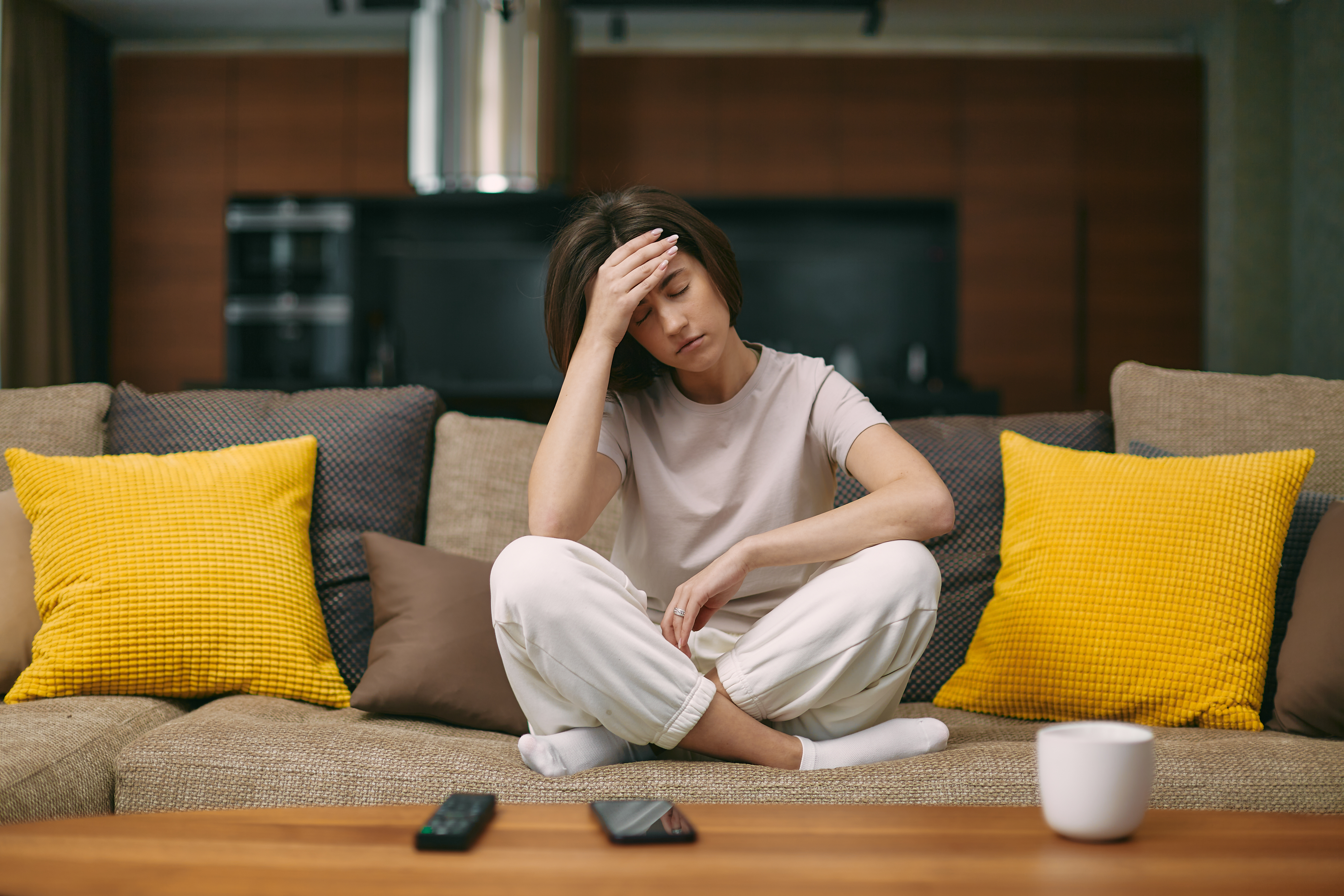 Young woman sitting on her sofa with her hand on her head looking tired.