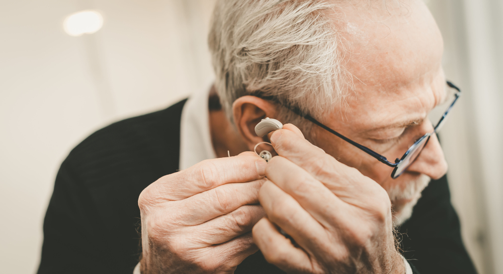 Older man places a hearing aid in his ear. 