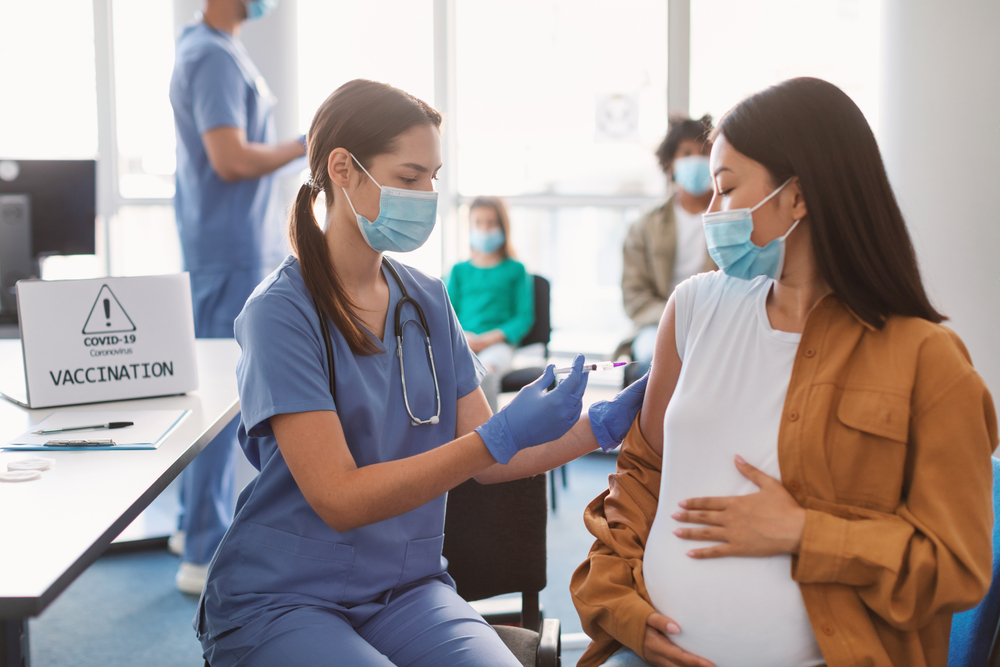 Pregnant woman in face mask receiving a vaccine.