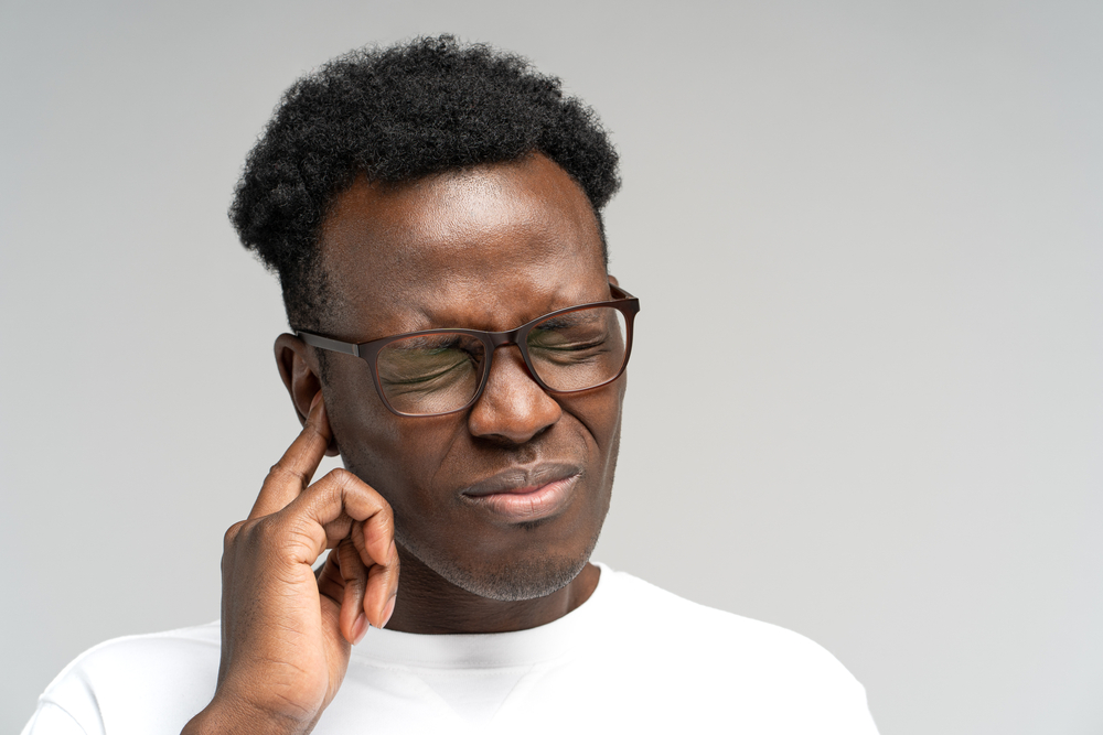 Young Black man touching his ear in distress.