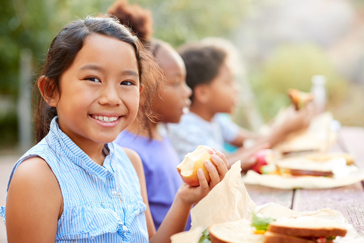 Smiling girl with friends eating at a picnic