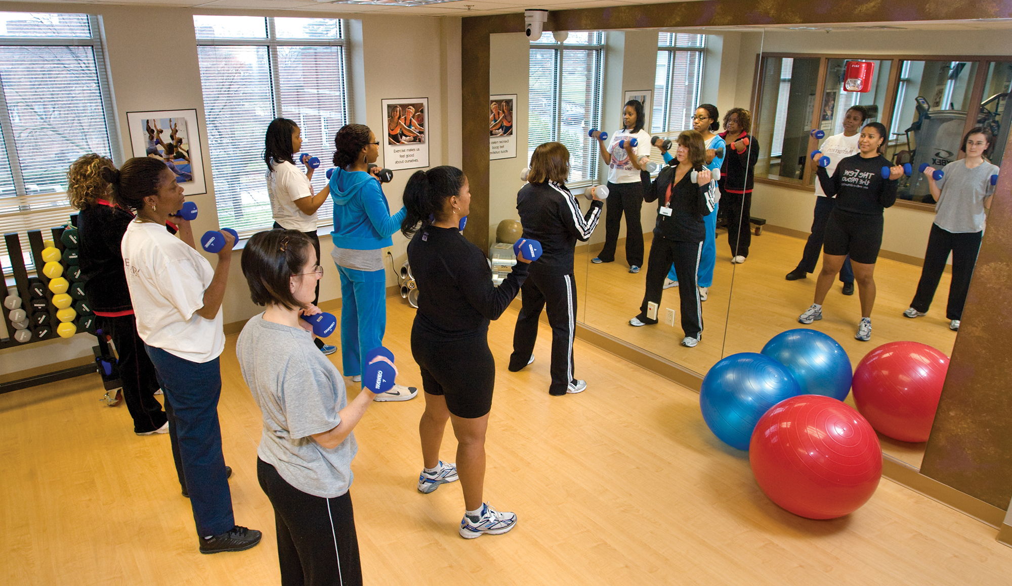 Women in a class working out with dumbbells in front of a mirror.