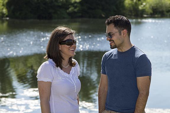 A young happy couple talking and smiling by a lake.