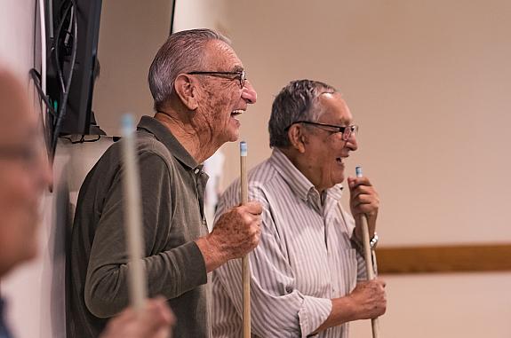 Two older men speaking to each other while holding pool cues.