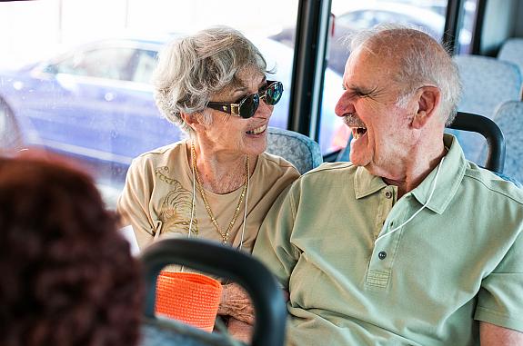 Two people riding on a bus smiling at each other.