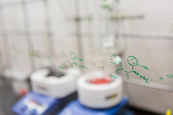 Chemical structures drawn on a glass pane in front of lab equipment