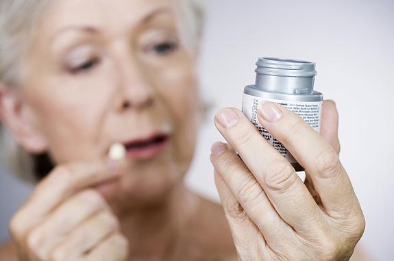 Older woman holding a single tablet and looking at a bottle of aspirin.