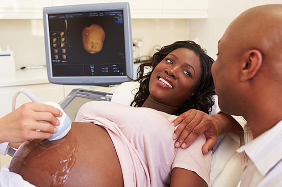 Pregnant woman getting an ultrasound while smiling at a man who has his hand on her shoulder.