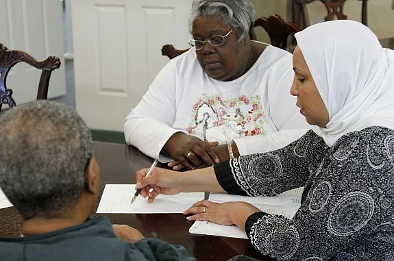 A female healthcare worker is speaking with two individuals while sitting at a table together.