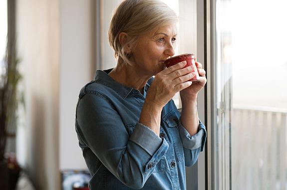 Senior woman looking out a window sipping a cup of tea