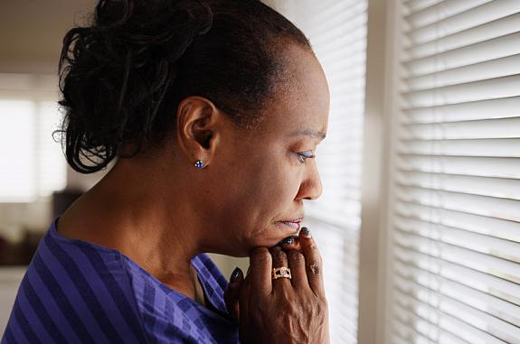 An older black woman mournfully looks out a window.