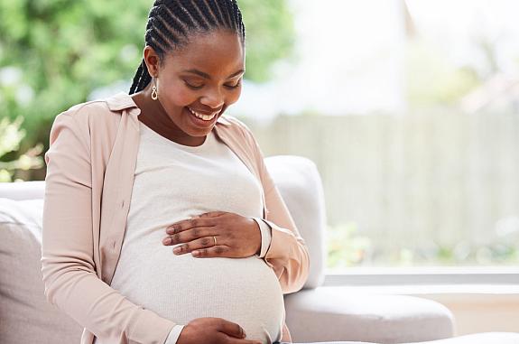 Pregnant woman on sofa smiling down at her belly.