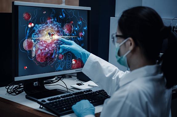A researcher pointing to a molecular structure on a computer monitor.