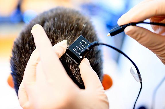 Researcher plugging a cable into a device on a person’s head.