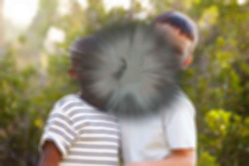 Two boys whose faces cannot be seen because the center of the image contains a greyish splotch. The image illustrates how a person with AMD has a diminished ability to see objects or people in their central vision.
