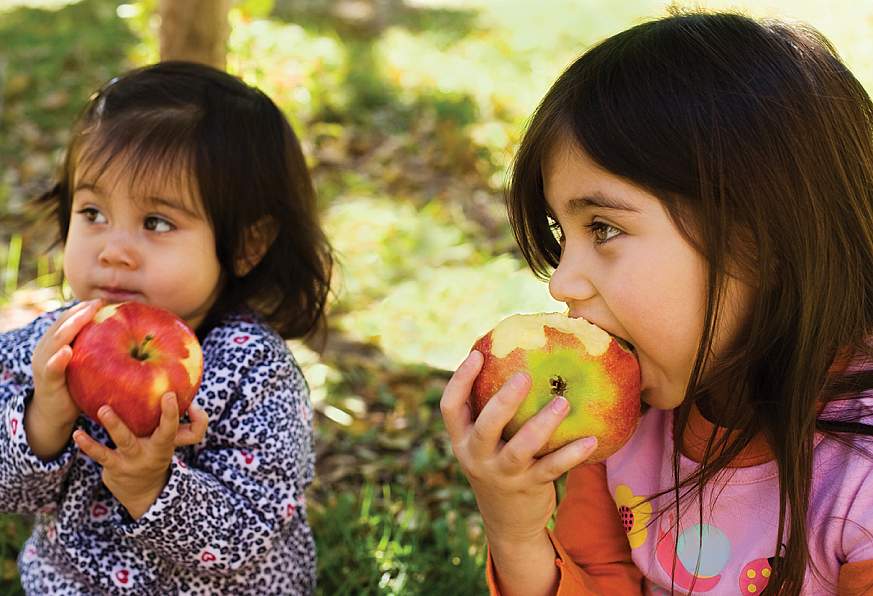 Two young girls eating apples outside.