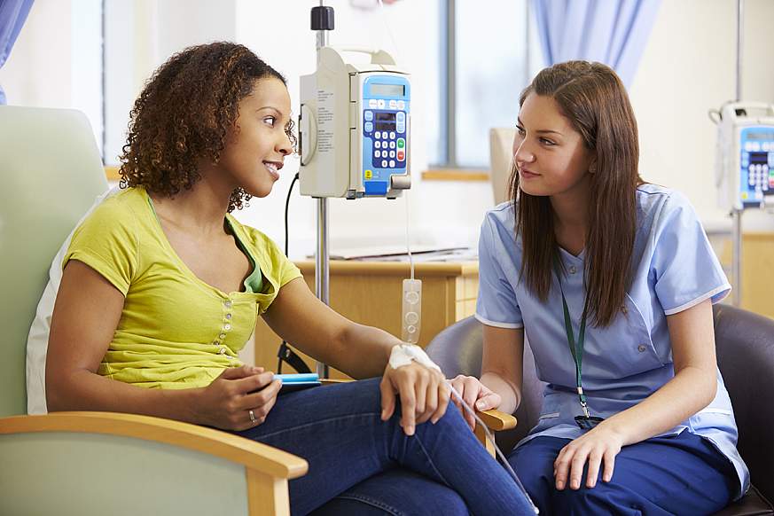 Inclusion in Clinical Trials Female patient and female nurse sit looking at each other while the patient has an IV in her hand.