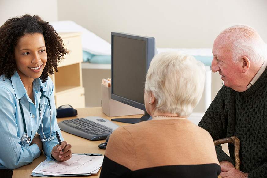 Female doctor talking to a senior couple at her desk.