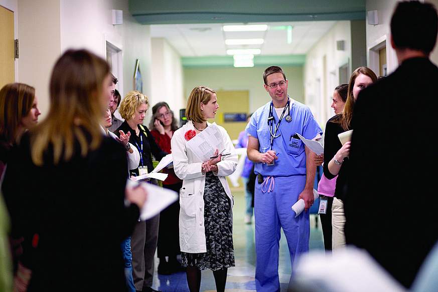 Two doctors in a hospital hallway surrounded by people.