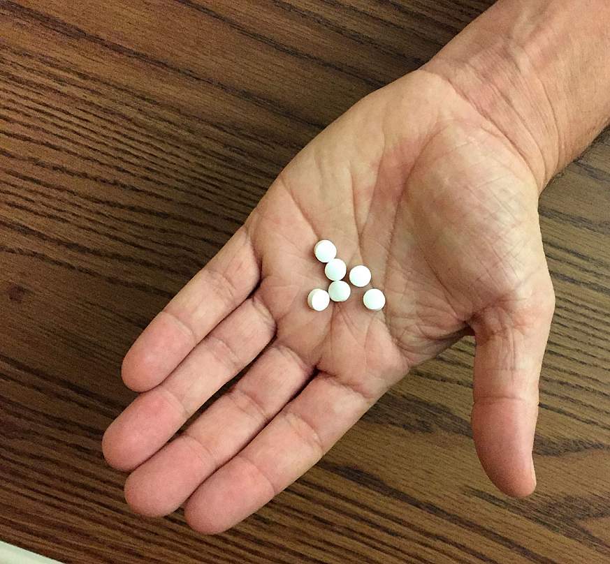 Hand holding six white pills