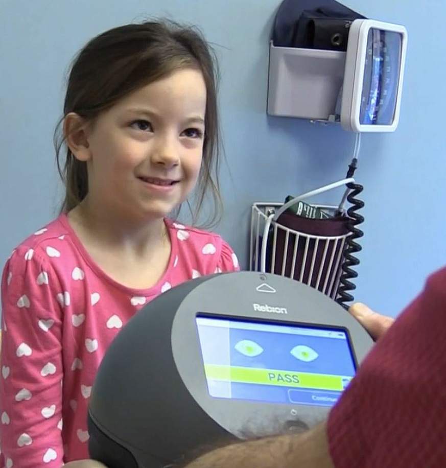Female child smiles facing person holding screening device in a medical setting