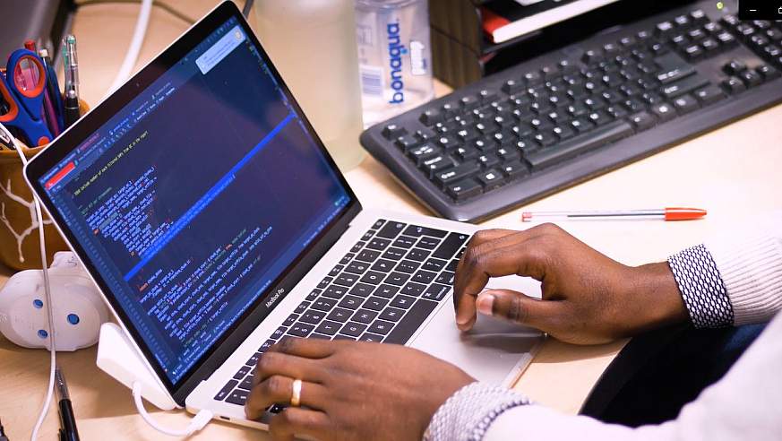 hands typing on a laptop with data on screen and another keyboard nearby