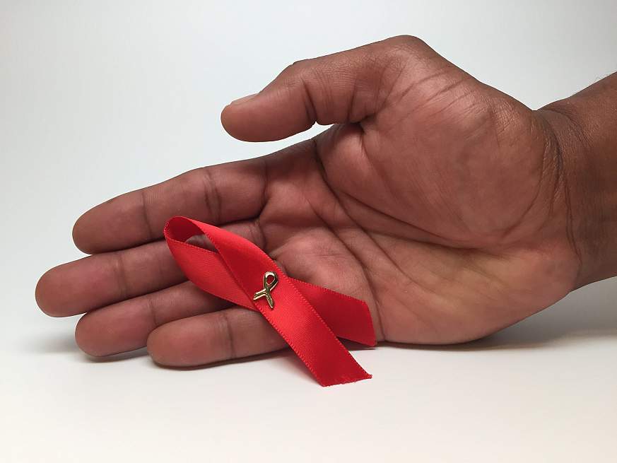 An HIV awareness ribbon in a person's hand.