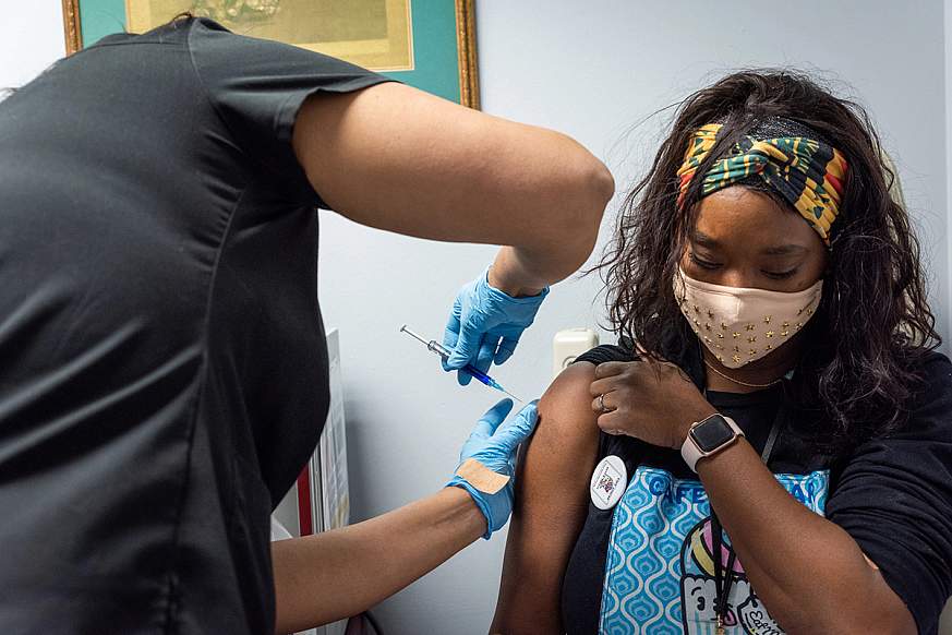 Healthcare worker administers a vaccine to upper right arm of seated volunteer.