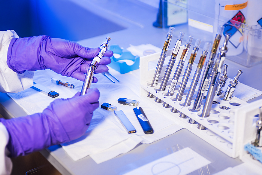 Gloved hands of lab technician conducts research on electronic cigarettes, or e-cigs, and vaping pens, inside a laboratory environment