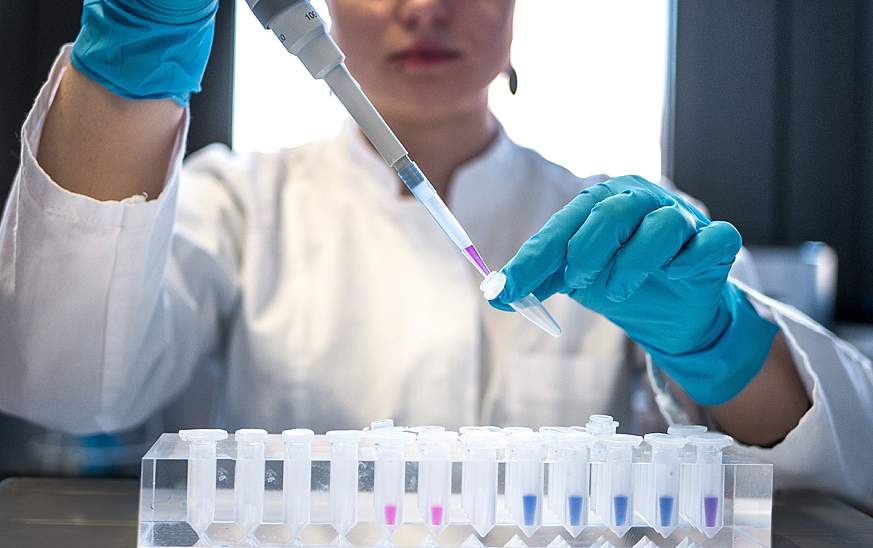 Scientist wearing blue gloves uses pipette to put fluid in tube. 