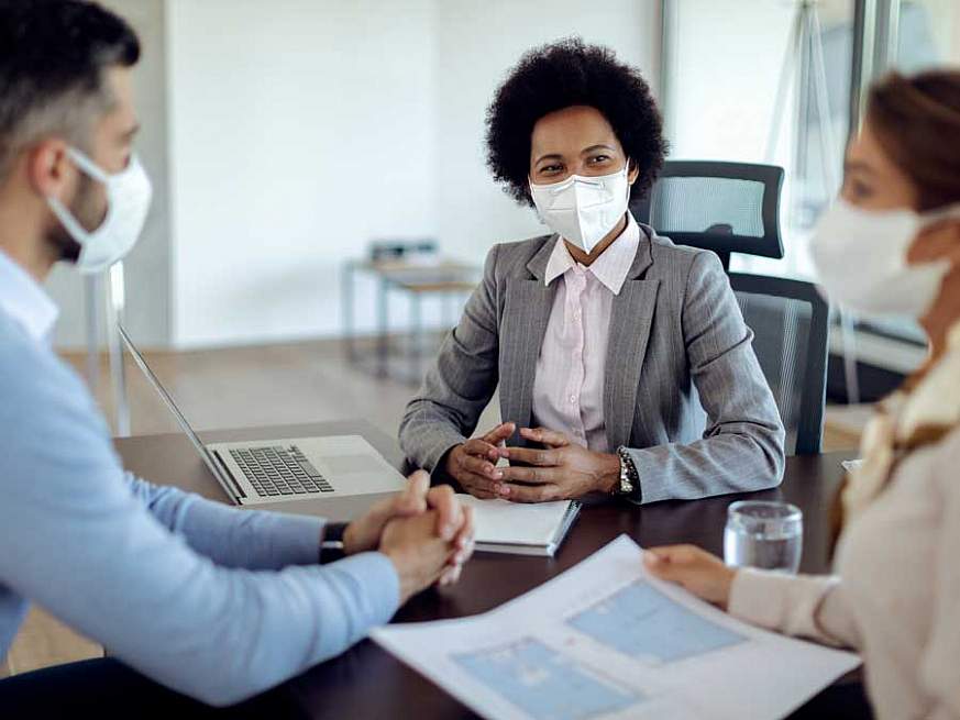 Three seated professionals wearing medical face masks collaborating in an office table.