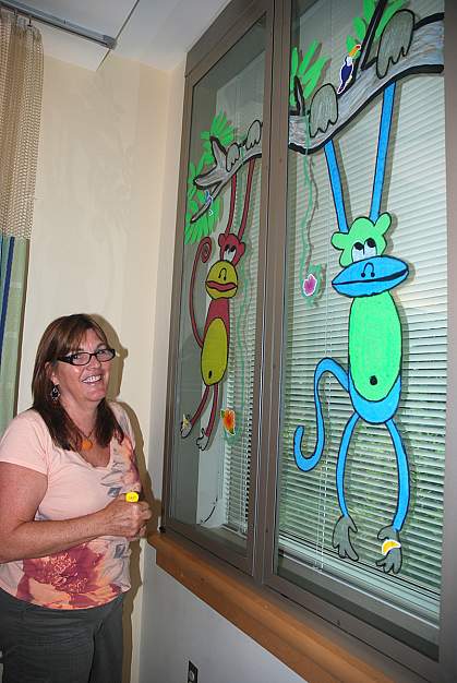 Annette Weller, a self-taught artist, shows a monkey tree she painted on a Clinical Center window.