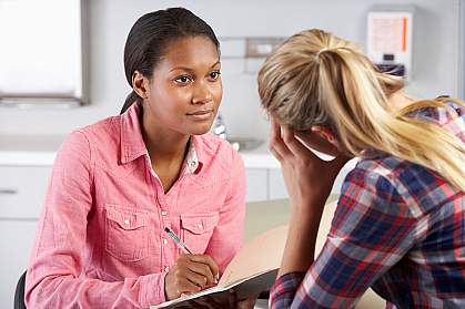 A woman taking notes as she interviews another woman.