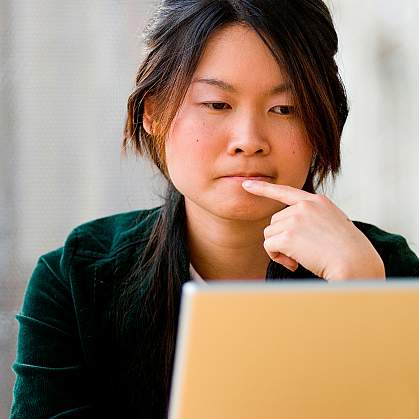 A young woman thinking as she looks at a laptop computer screen.