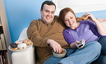 An overweight couple on the sofa eating popcorn.