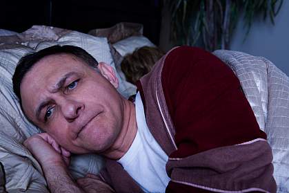 Photo of an angry man lying awake in bed