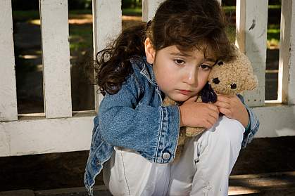 Photo of a young girl looking sad, hugging a teddy bear