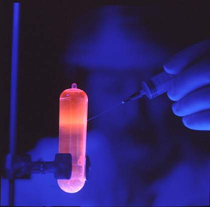 Under blue light, researcher uses a syringe to extract purified DNA, which glows orange, from a tube